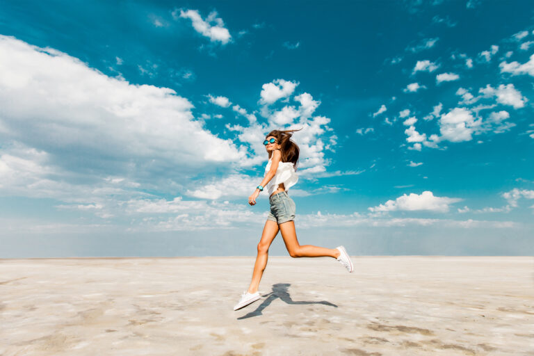 happy-young-fresh-slim-athletic-girl-runs-along-beach-trendy-jeans-shorts-white-sneakers-blue-sky-clouds-summer-sunny-mood